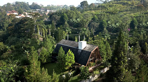 Secluded forest cabin with modern architecture nestled among lush green trees and rolling hills, showcasing innovative design and integration with natural surroundings.