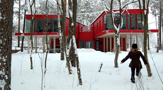Modern red minimalist house surrounded by snow-covered trees in winter.