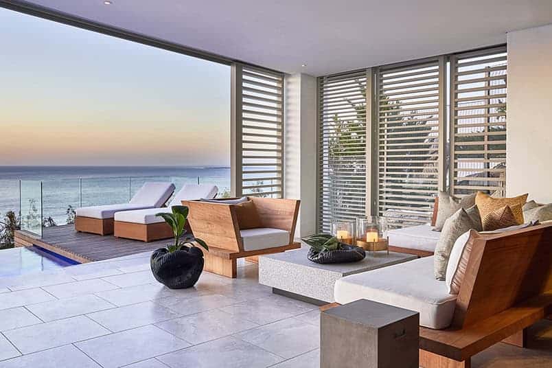 Modern ocean view living room with minimalist design, wooden furniture, and large windows showcasing seaside scenery. Perfect for luxury beach house interior design and architecture.
