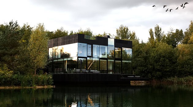 Modern black glass luxury house with waterfront view, contemporary architectural design, surrounded by lush greenery, ideal for modern living and scenic outdoor environments.