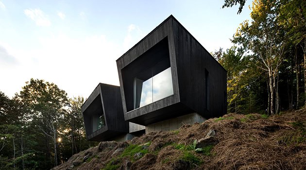 Modern black cube houses with large window openings on a hillside surrounded by trees, showcasing innovative contemporary architecture and unique design elements.