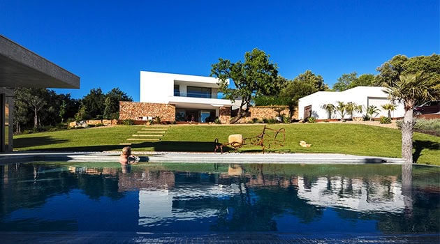 Modern minimalist architectural house with sleek white facade and clean lines, set in lush greenery and featuring a stunning outdoor pool area.