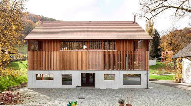 Sustainable modern wooden house with a concrete foundation, featuring large windows and a sloped roof, set in a scenic autumn landscape.