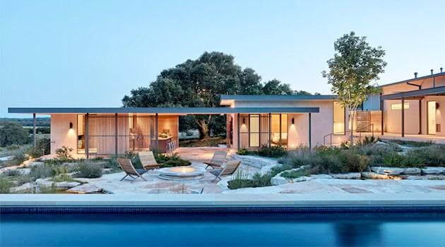 Modern minimalist single-story house with flat roof and large glass windows surrounded by landscaped yard and pool, showcasing contemporary architecture and outdoor living design.