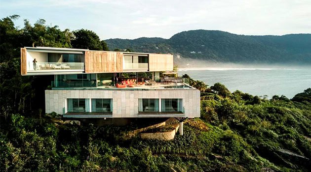 Stunning modern cliffside house with large glass windows and contemporary architectural design surrounded by lush greenery.