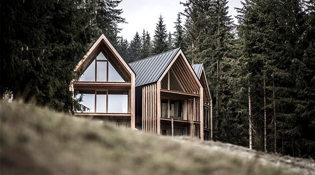 Modern wooden mountain cabin with large glass windows surrounded by tall pine trees for a rustic yet contemporary architecture design.