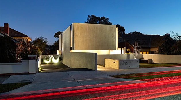 Contemporary minimalist residential architecture with sleek concrete walls and modern landscaping under evening sky, emphasizing innovative design and urban elegance.