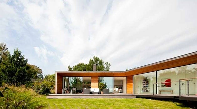 Modern minimalist house with large glass windows and wooden exterior overlooking lush greenery, highlighting contemporary architecture and sustainable design elements.