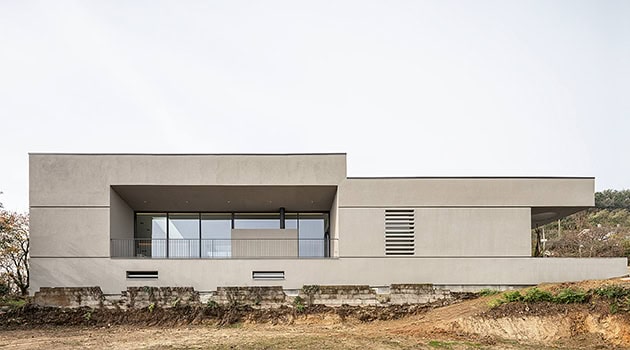 Modern minimalist concrete house with large glass windows and clean architectural lines, located on a slightly elevated terrain, showcasing contemporary design and innovative architecture.