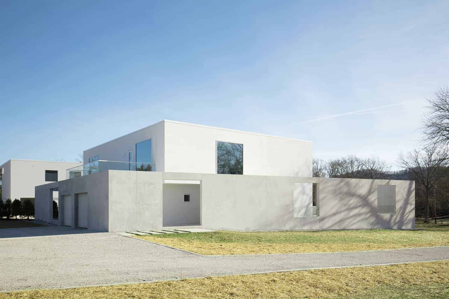 Minimalist modern white house with geometric design, large windows, and clean lines, surrounded by a landscaped lawn and clear blue sky. Perfect example of contemporary architecture and innovative home design.