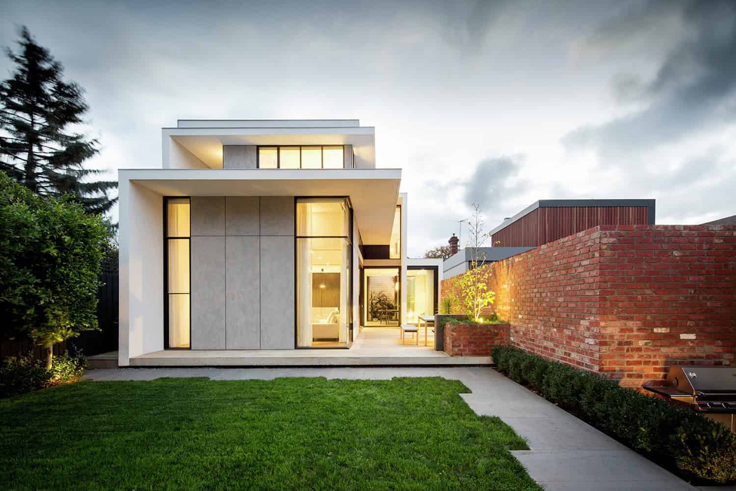 Contemporary modern house with minimalist architectural design, large glass windows, and sleek exterior, surrounded by a lush green lawn and outdoor lighting for stylish residential architecture.