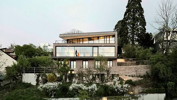 Modern contemporary house with large glass windows and lush hillside surroundings, showcasing innovative architectural design and stunning eco-friendly landscape integration.