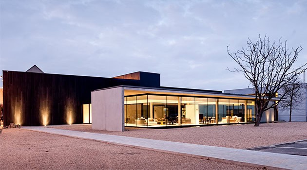 Modern minimalist house with large glass windows and sleek design, featuring a combination of concrete and wood exterior.