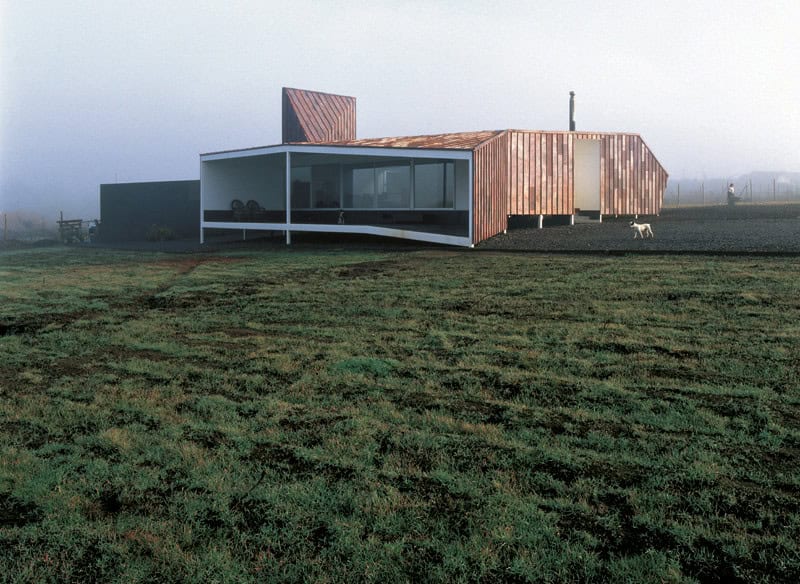 Modern minimalist house with wood and glass elements in a rural landscape.
