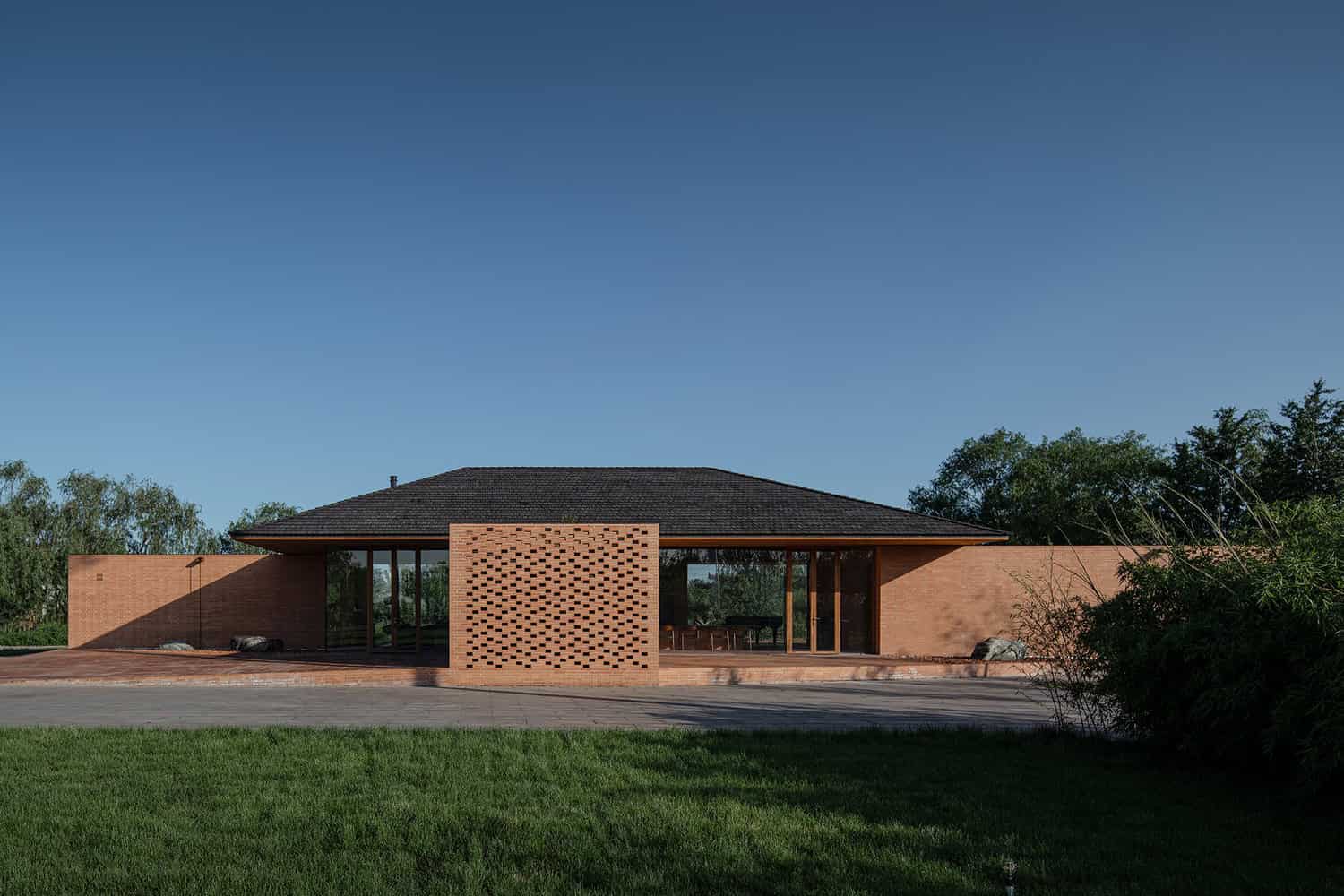 Modern single-story house with brick exterior, large glass windows, and a minimalist design set against a clear blue sky.