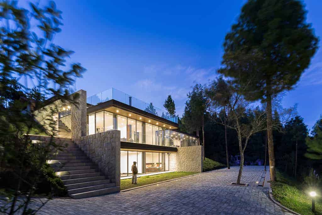 Contemporary modern house design with extensive glass windows, natural stone accents, and integration with lush surrounding landscape, showcasing innovative architecture and elegant design.