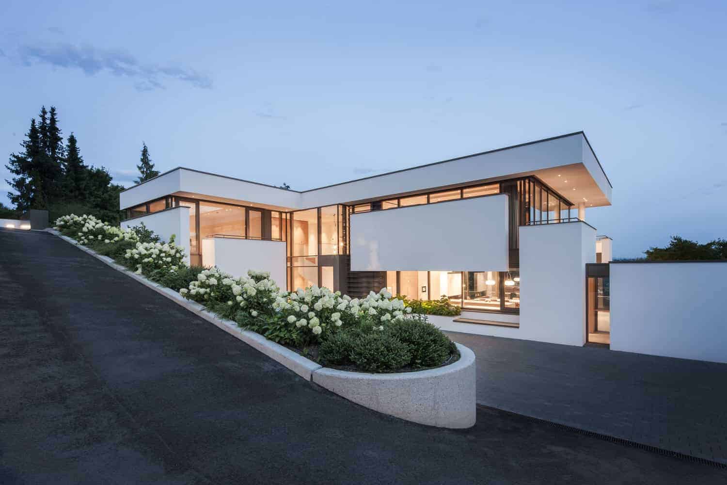 Modern luxury house with minimalist white exterior, large glass windows, and sleek architectural design, surrounded by landscaped garden and blooming white hydrangeas.