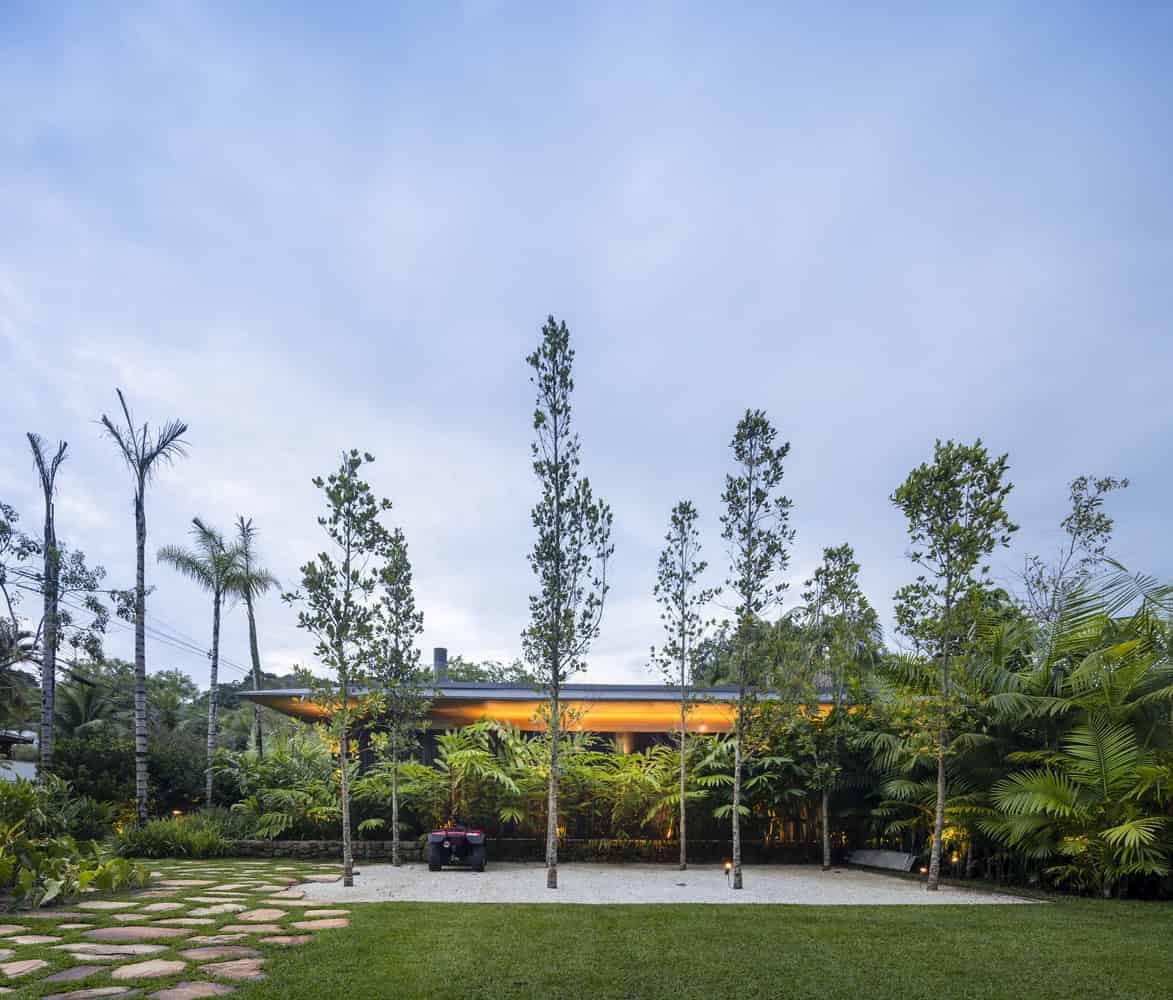 Lush tropical garden with modern architecture home surrounded by tall trees and vibrant greenery. Stylish landscape design featuring stepping stones and ambient lighting enhances the contemporary outdoor space.