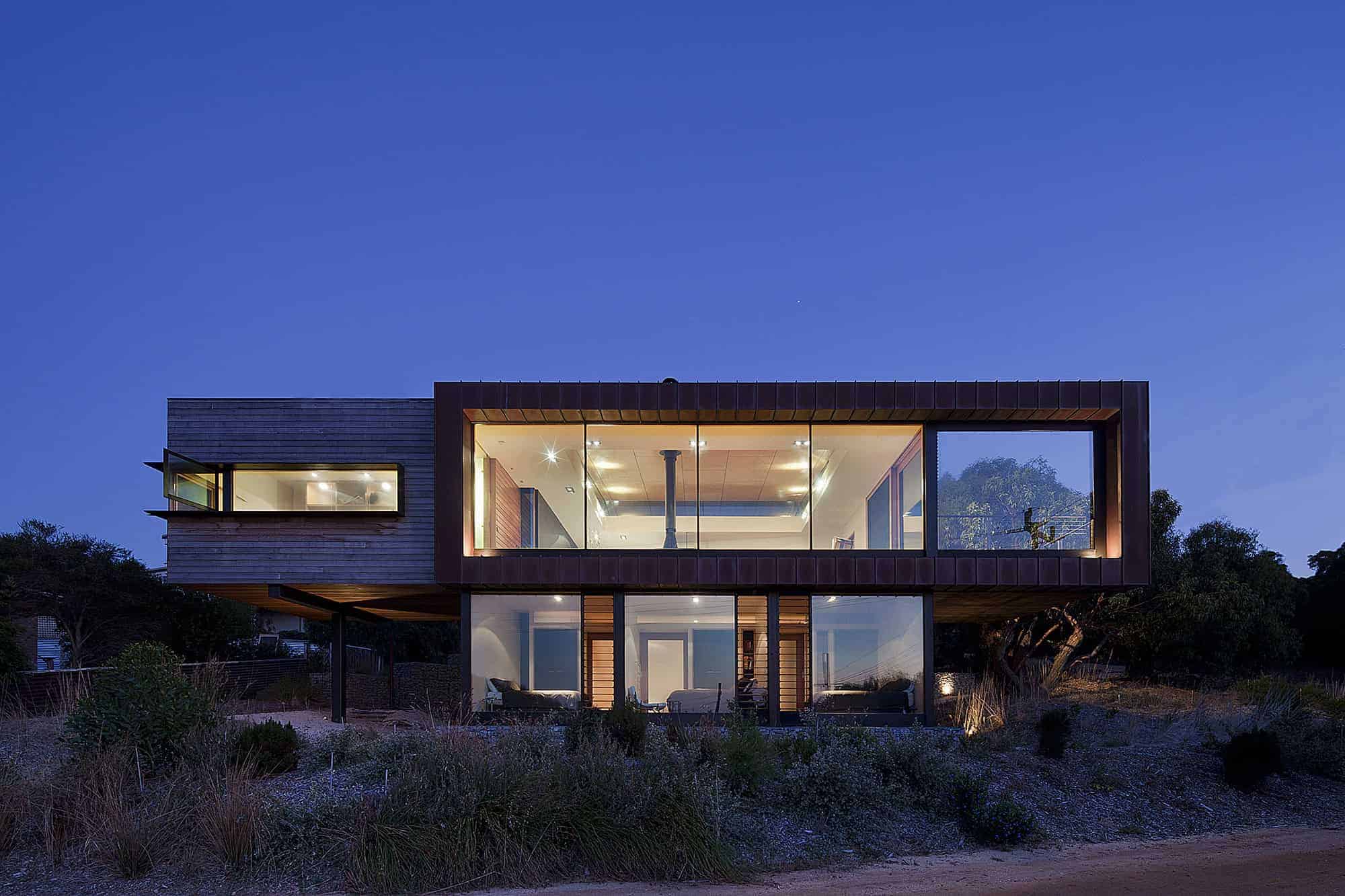 Contemporary modern house with large glass windows, wooden exterior, and sleek architectural design, set on a hillside with natural landscaping, exemplifying innovative architecture and stylish home design.
