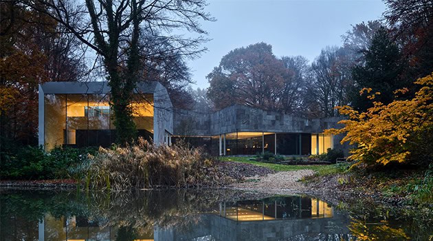 Modern glass house with sleek architectural design surrounded by nature and a pond reflection, showcasing contemporary architecture and innovative building techniques.