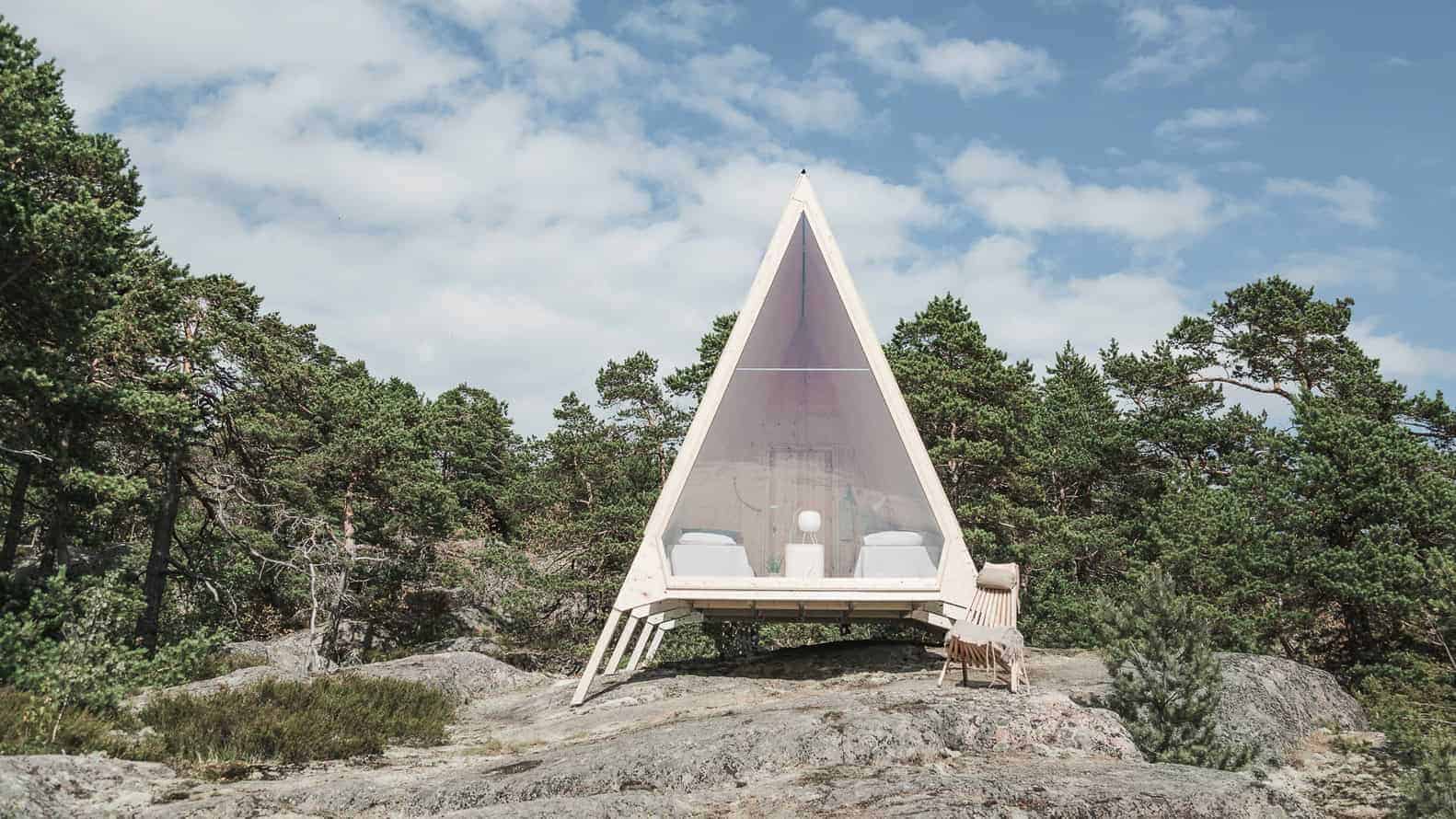 Modern A-frame glass cabin nestled in forest, minimalist tiny house with panoramic windows, eco-friendly retreat in nature, unique architecture blending with natural surroundings.