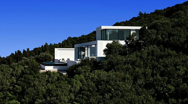 Contemporary modern house with large glass windows on a hillside surrounded by lush greenery; luxury architecture design.