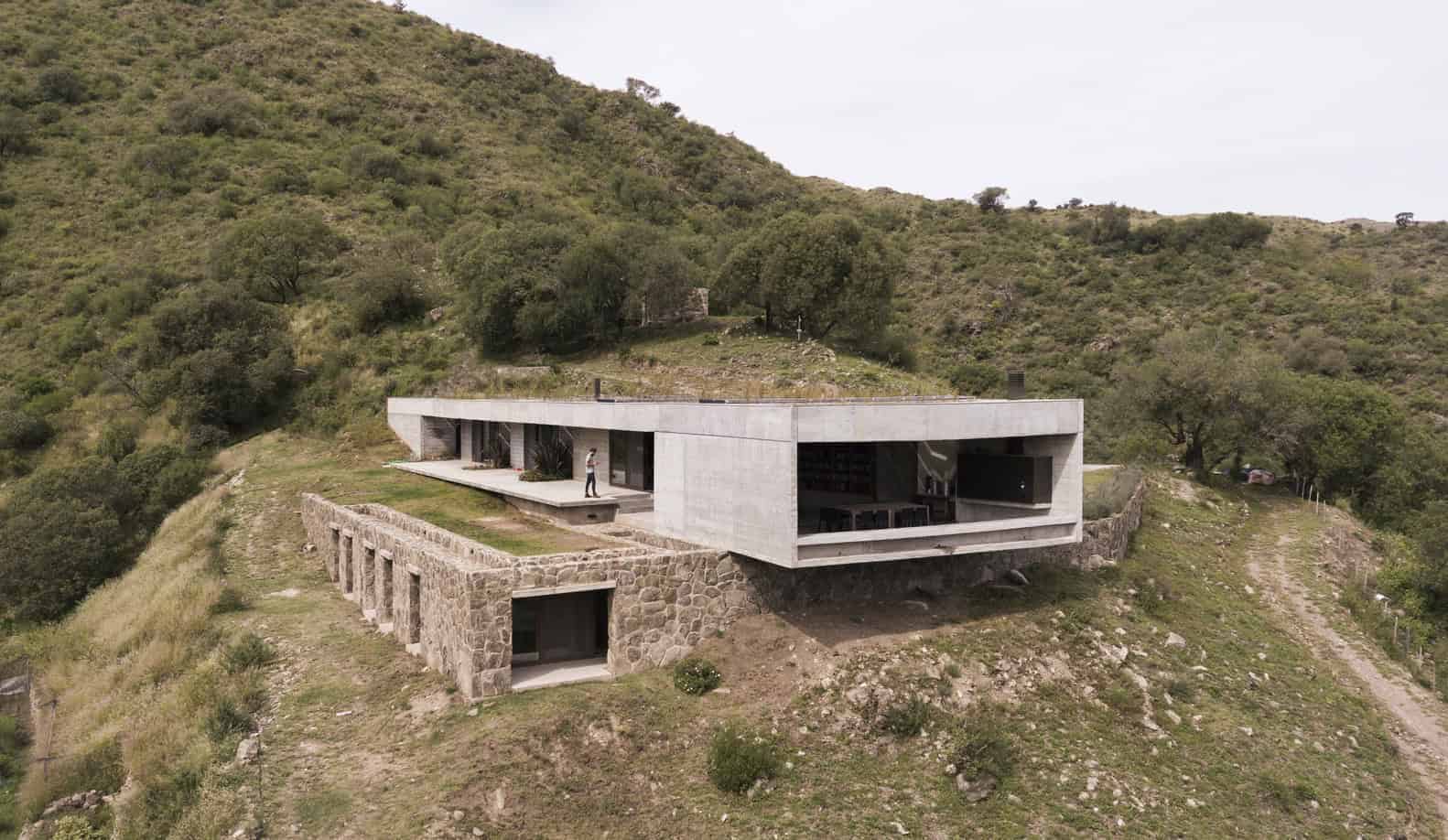 Modern hillside house featuring sleek concrete and stone architecture integrated with natural landscape, offering stunning panoramic views and eco-friendly design.