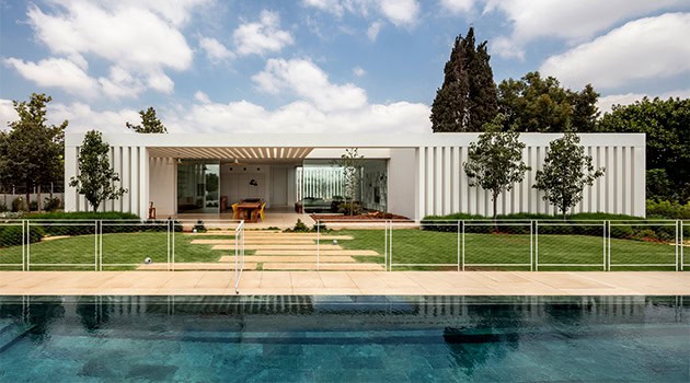 Modern minimalist white house with clean lines and large glass windows, seamlessly blending indoor and outdoor living spaces in a luxurious setting.