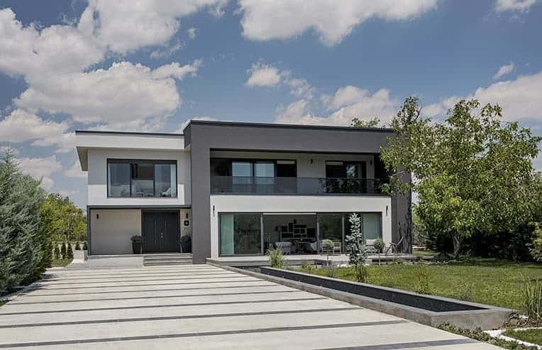 Modern two-story house with sleek architectural design, large windows, and contemporary exterior in a lush green landscape.