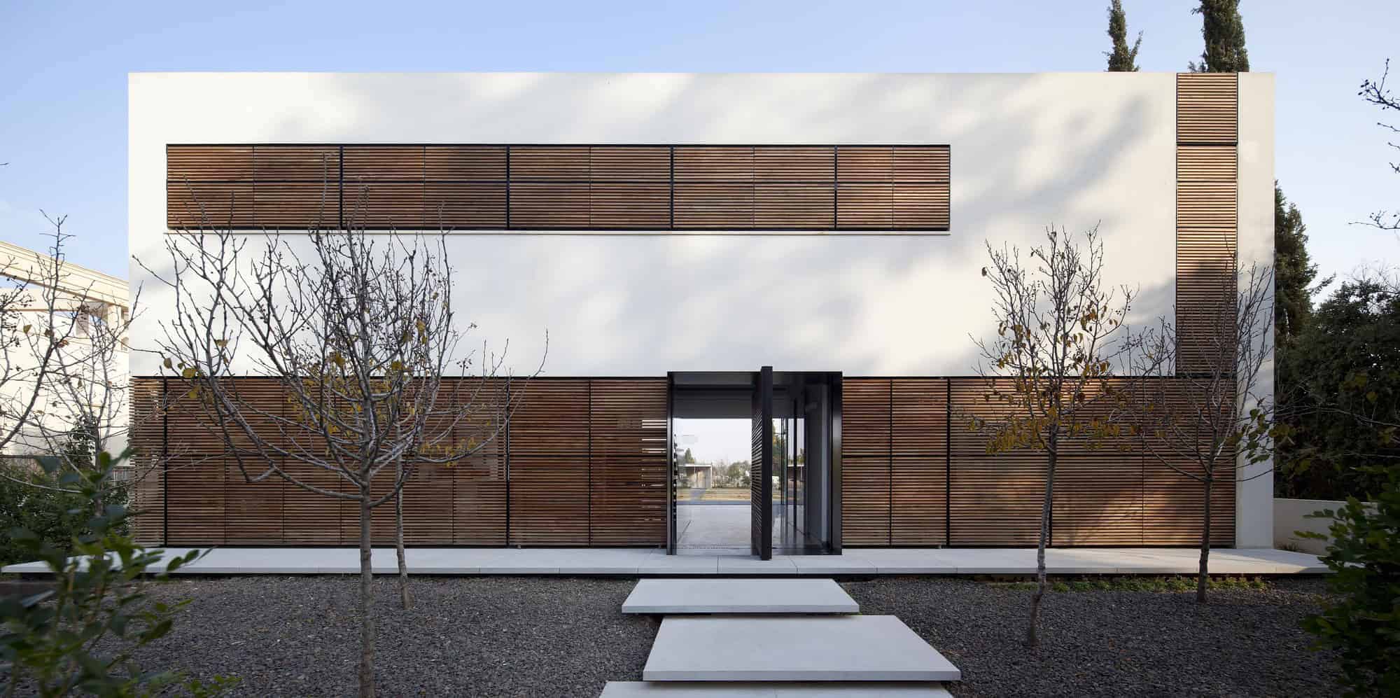 Contemporary modern house with wooden slats and minimalist design, featuring clean lines and a sleek entrance, surrounded by minimalist landscaping and trees.