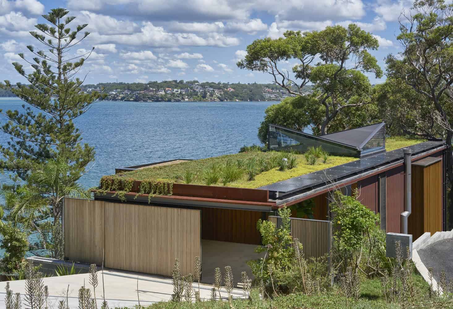 Contemporary eco-friendly house with green roof overlooking a scenic water body and lush trees, emphasizing modern sustainable architecture and outdoor integration.