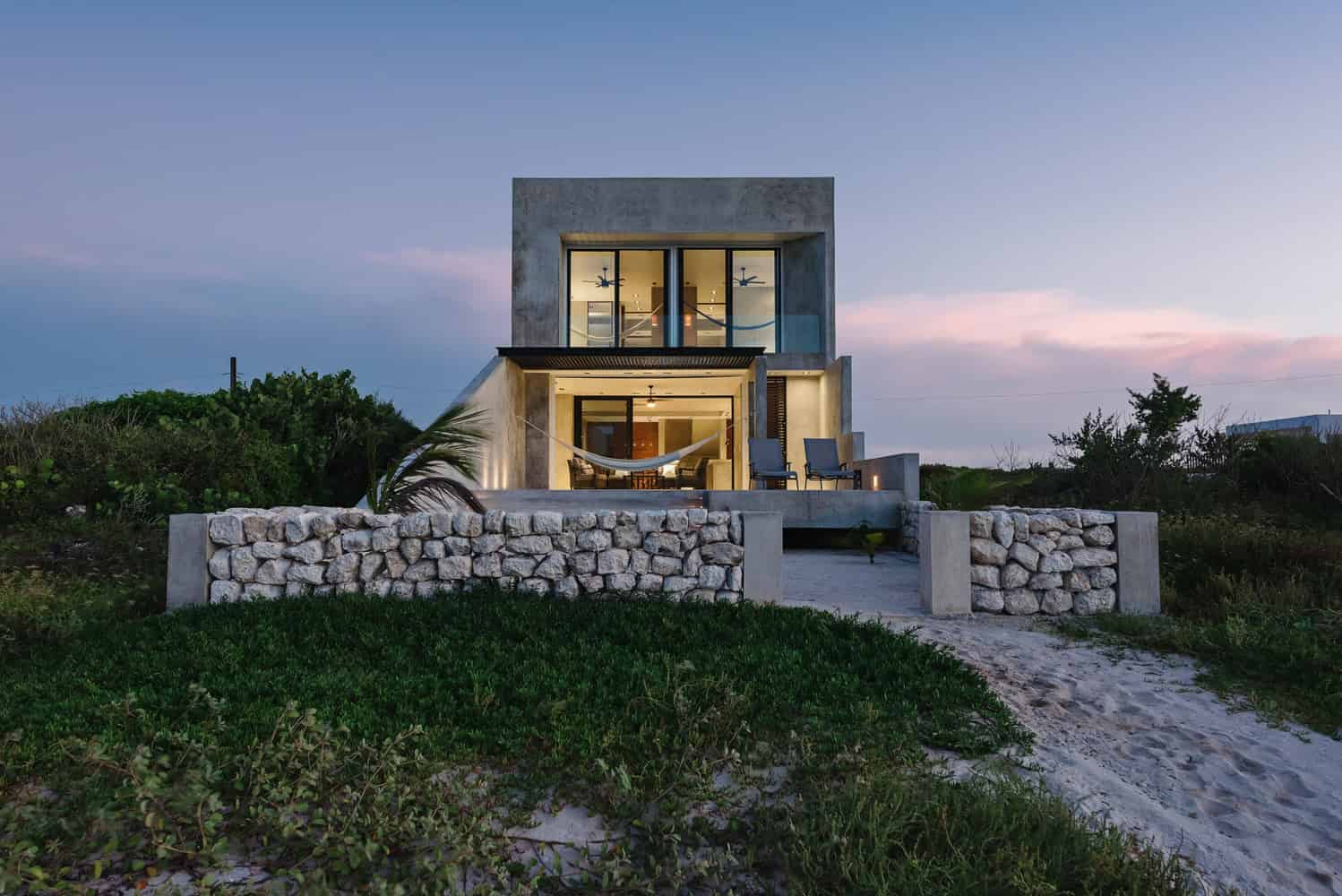 Modern beachfront house with concrete and stone accents, outdoor patio, and tropical landscaping, showcasing contemporary architecture and design.