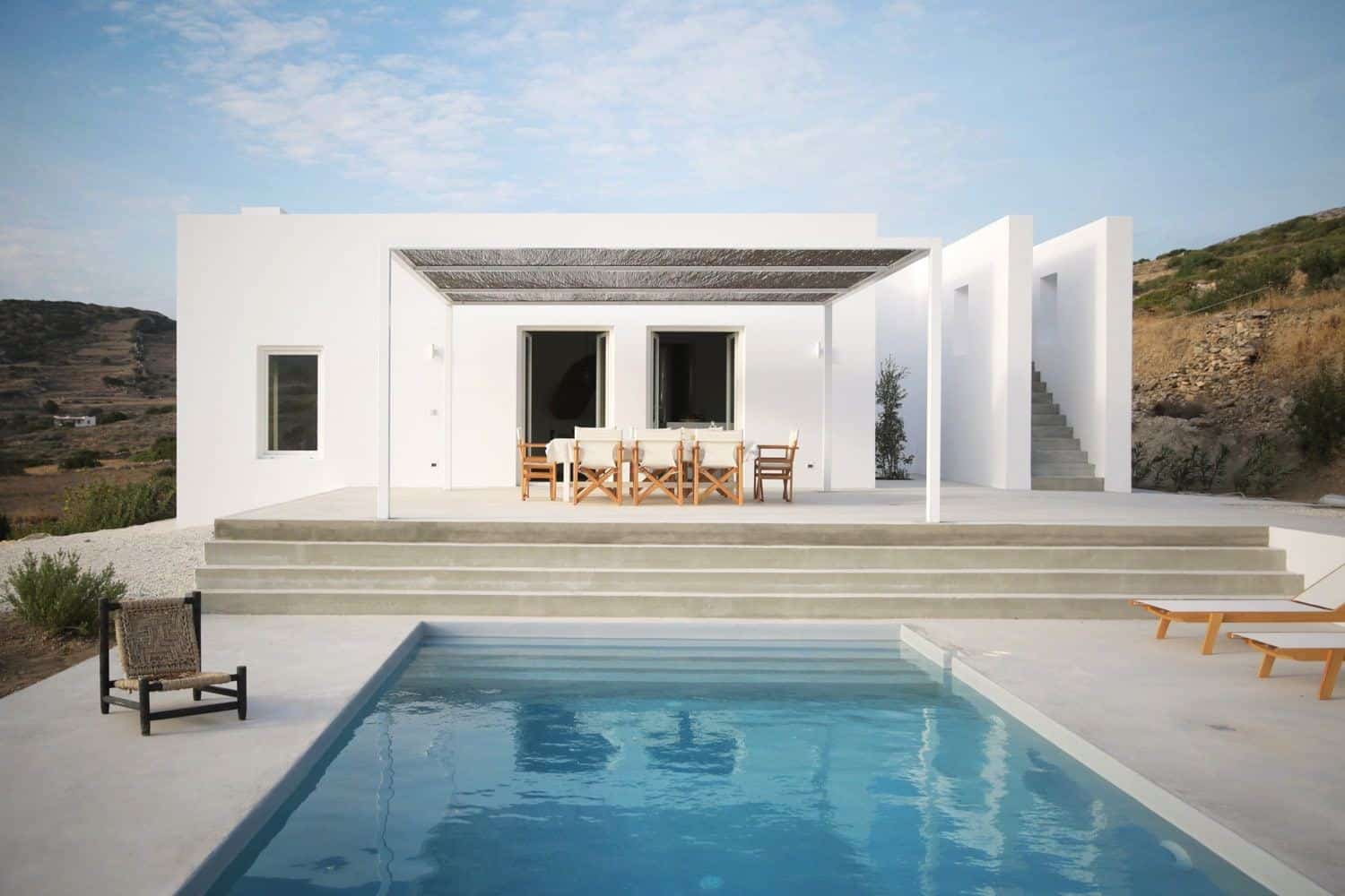 Modern minimalist white villa with outdoor dining area, infinity pool, and mountain-view landscape, exemplifying contemporary architecture and stylish outdoor living spaces.