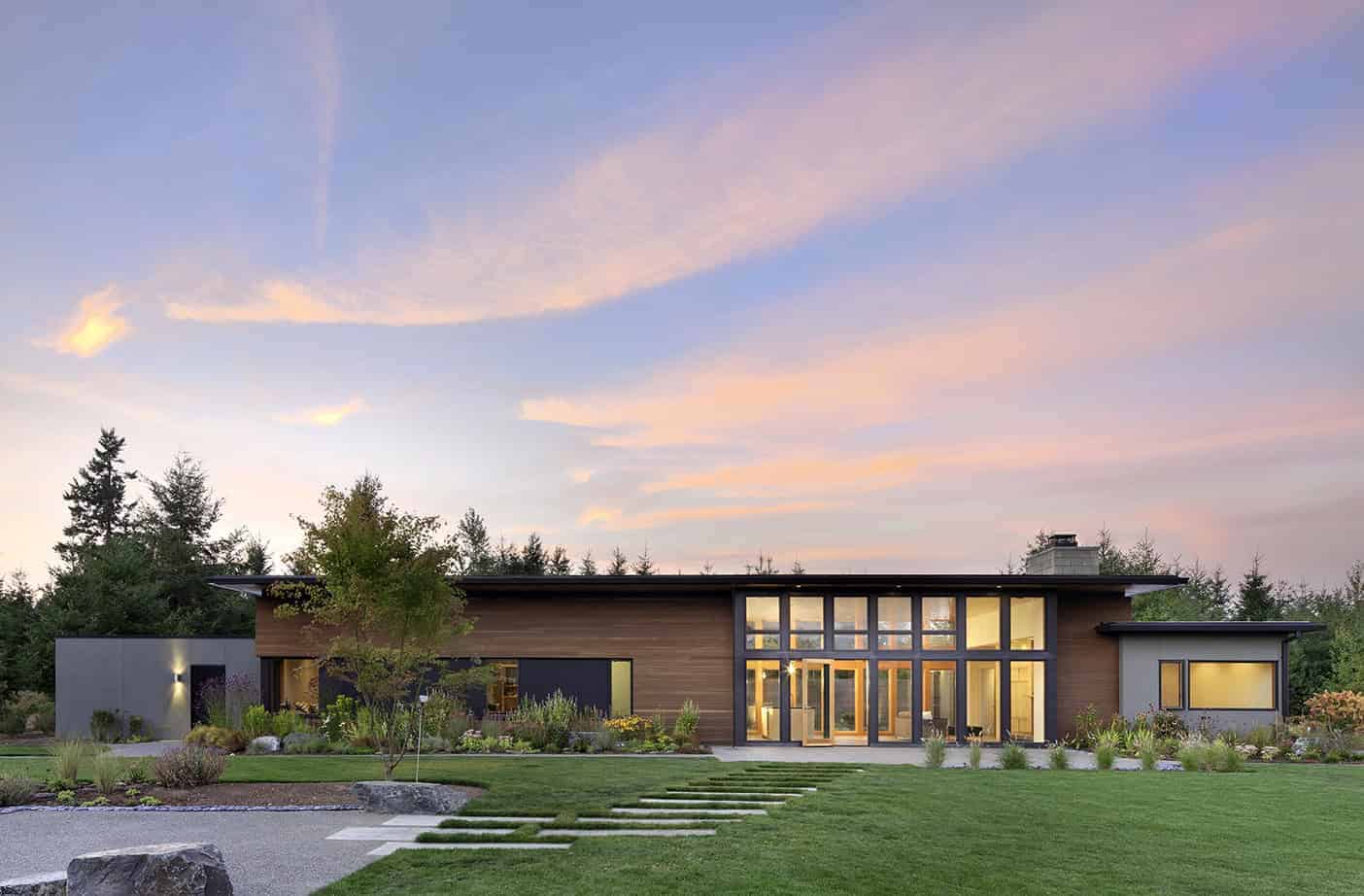 Contemporary modern house with large glass windows, wooden siding, and landscaped yard during sunset, showcasing minimalist architectural design and eco-friendly outdoor landscaping.