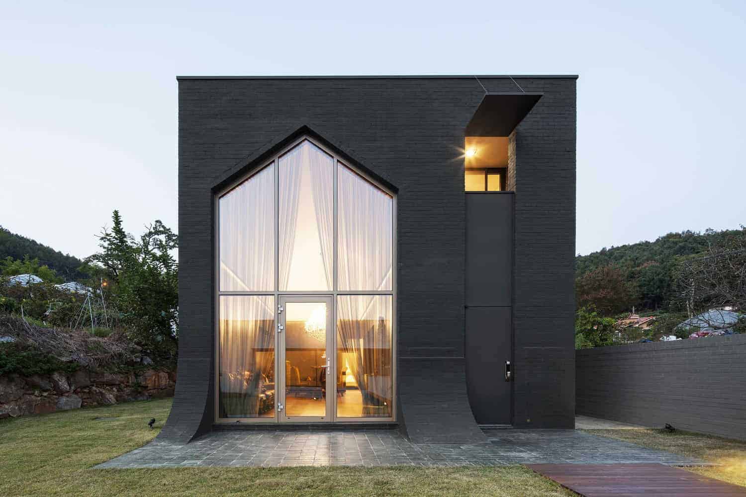 Contemporary black modern house with large glass windows and unique architectural design, set against a scenic hillside background, showcasing sleek minimalist architecture.