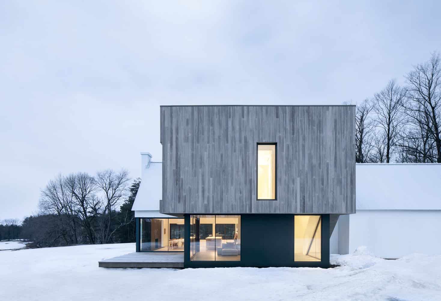 Contemporary modern house with minimalist design, wooden facade, and large glass windows in a snowy landscape.