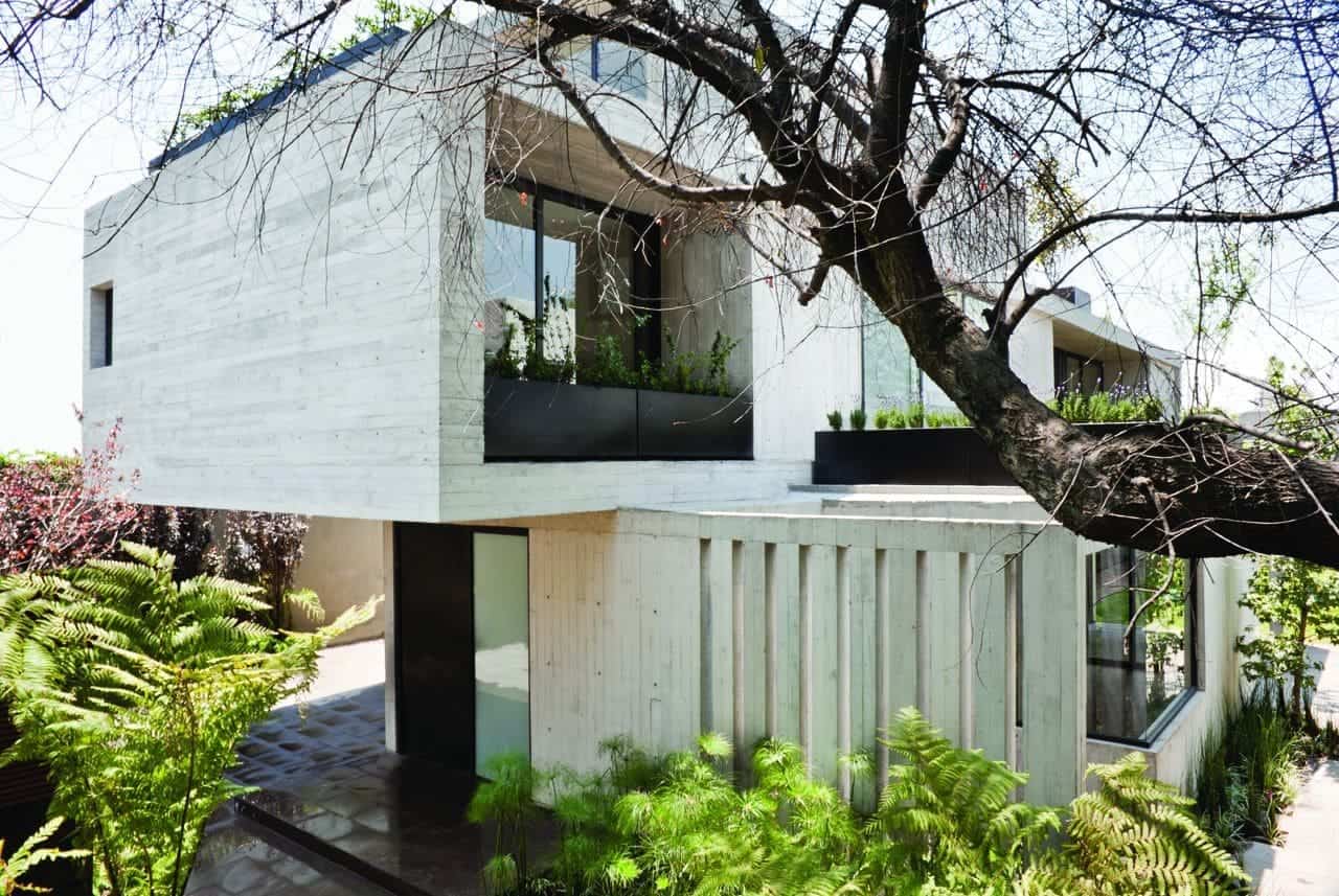 Modern minimalist concrete house with large glass windows and lush surrounding greenery, exemplifying innovative architecture and contemporary design.