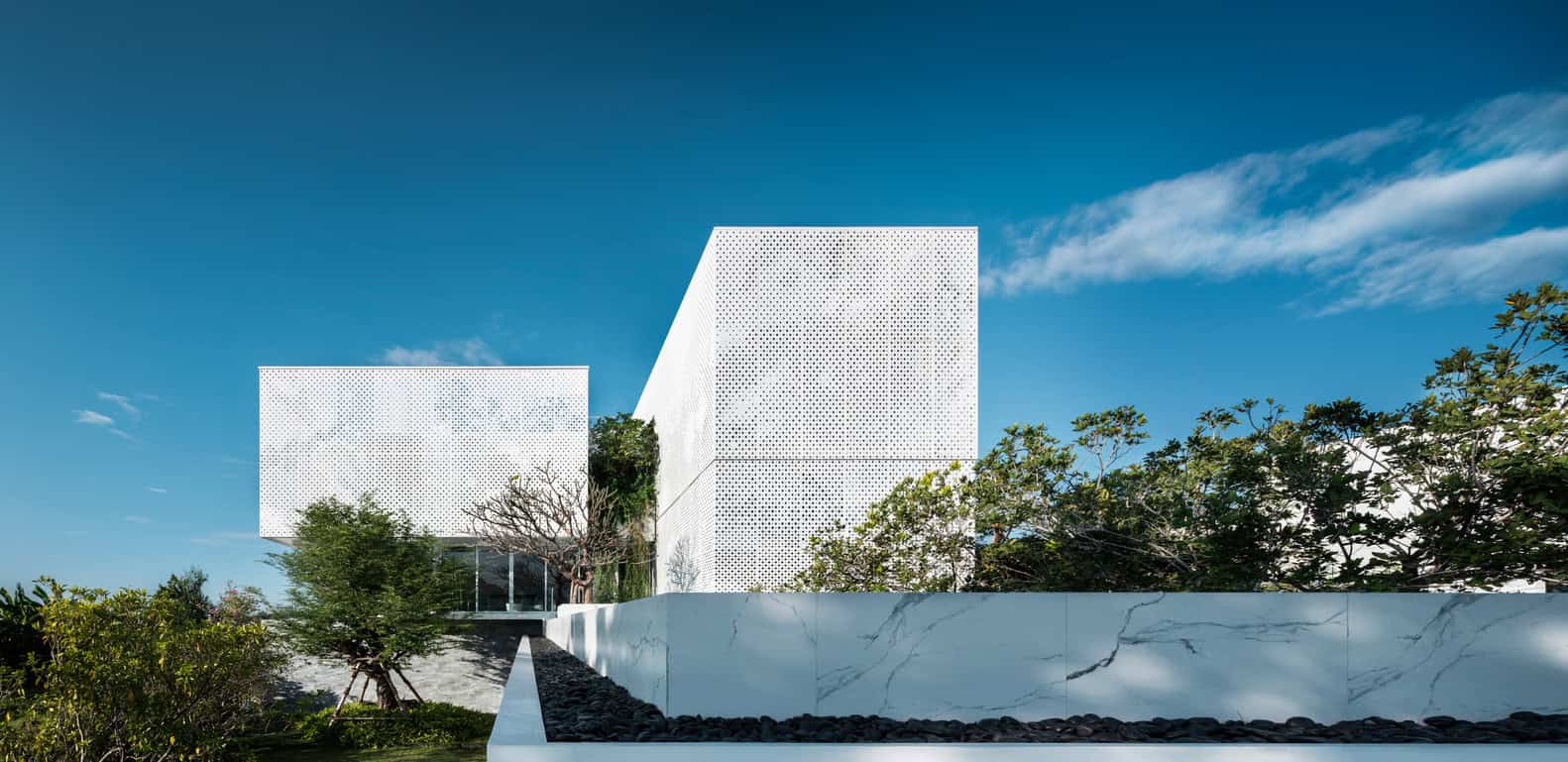 Modern minimalist architecture with sleek white perforated facade and lush landscaping, exemplifying contemporary design concepts and innovative building materials.