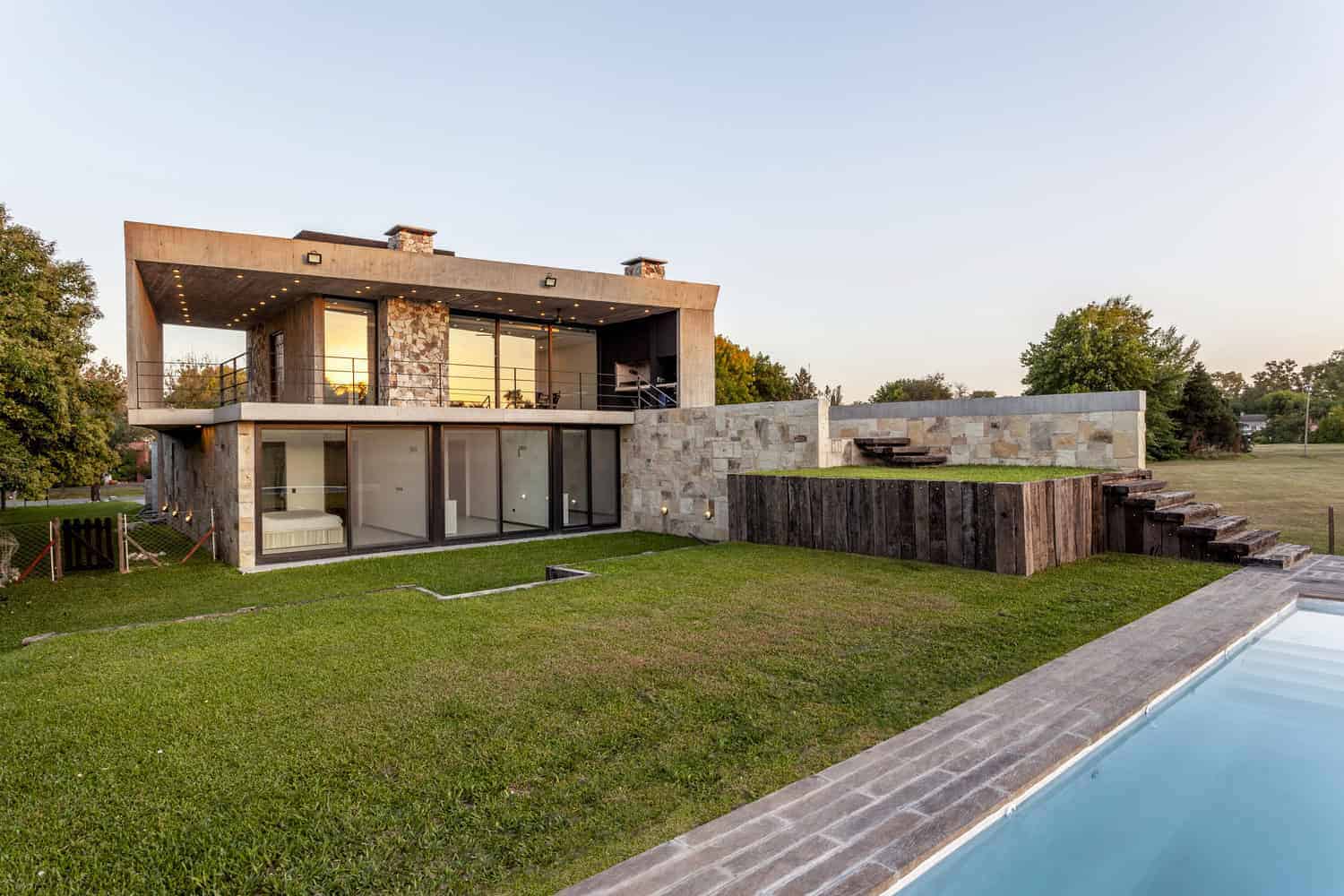 Contemporary modern house with large glass doors, stone accents, and a spacious backyard with a pool, showcasing innovative architecture and design.