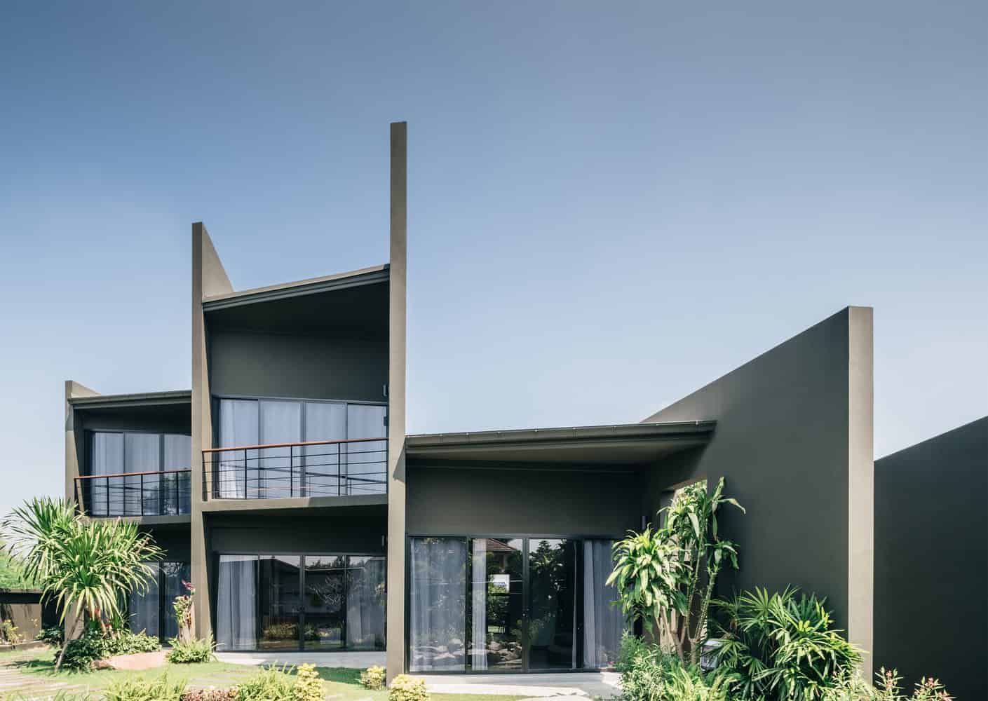 Futuristic modern house with sharp architectural design, sleek concrete exterior, large glass windows, and lush landscaping, showcasing innovative home architecture.