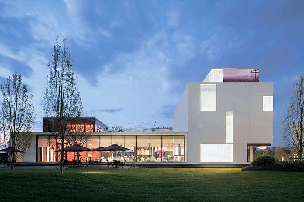 Futuristic modern architectural building with sleek white exterior and large glass windows, illuminated at dusk, showcasing contemporary design and innovative architecture art.