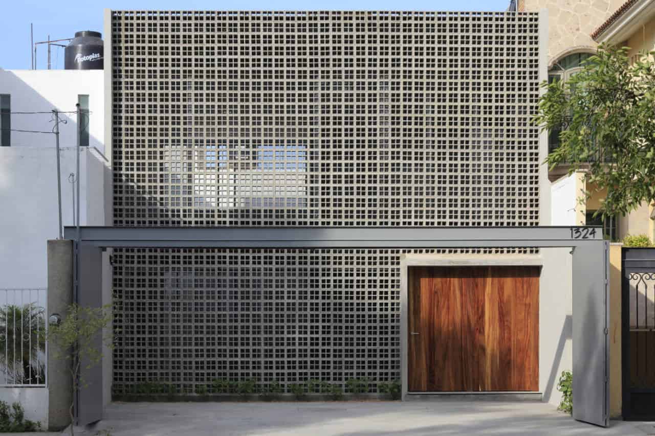 Modern residential façade featuring a unique concrete block wall design for ventilation and aesthetics, complemented by a wooden gate and contemporary urban architecture.