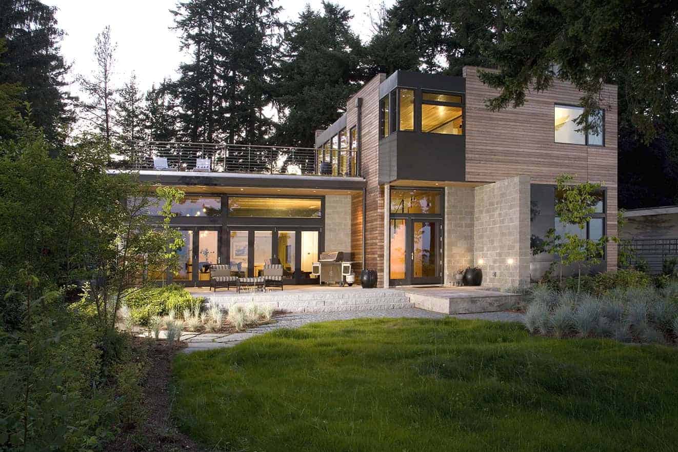 Contemporary modern house with spacious outdoor patio and large glass windows, surrounded by lush landscaping and tall trees, showcasing sleek architectural design and eco-friendly materials.