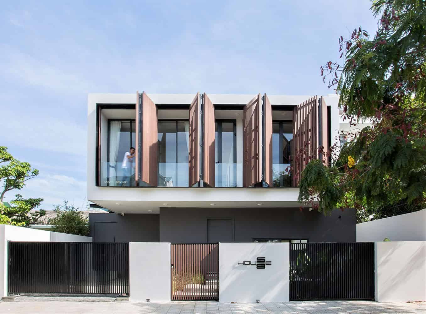 Contemporary modern house with unique wooden slatted facade design and large glass windows, set in an urban environment with greenery and sleek gate entrance.