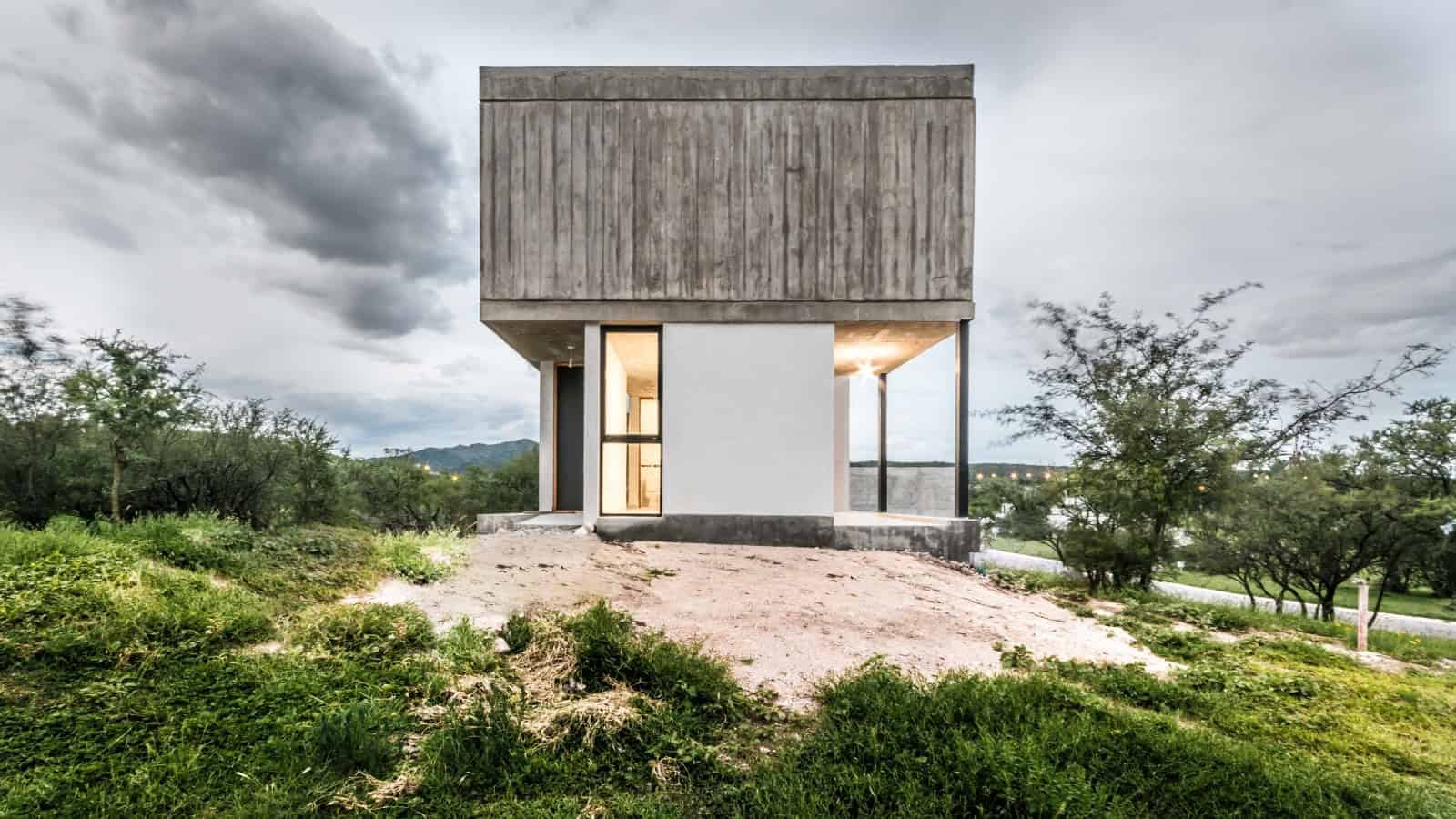 Modern minimalist concrete house with clean lines and large windows nestled in a lush green landscape.