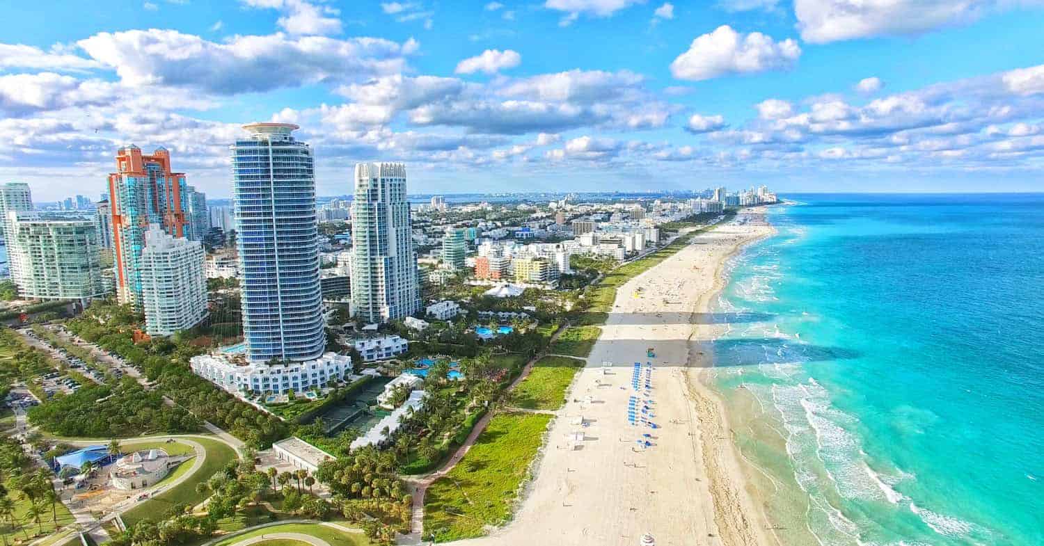 Modern beachfront city skyline with high-rise buildings and a pristine sandy beach under a partly cloudy sky, showcasing contemporary architecture and coastal scenery.