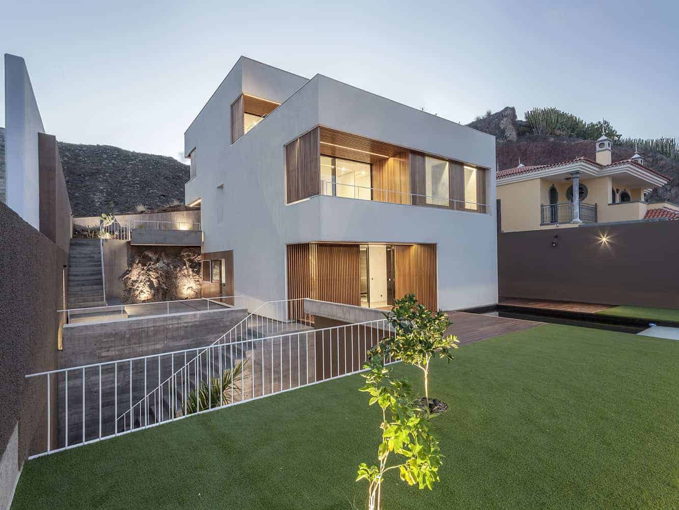 Contemporary modern house exterior with sleek white facade, wooden accents, large glass windows, and landscaped yard showcasing innovative architecture design.