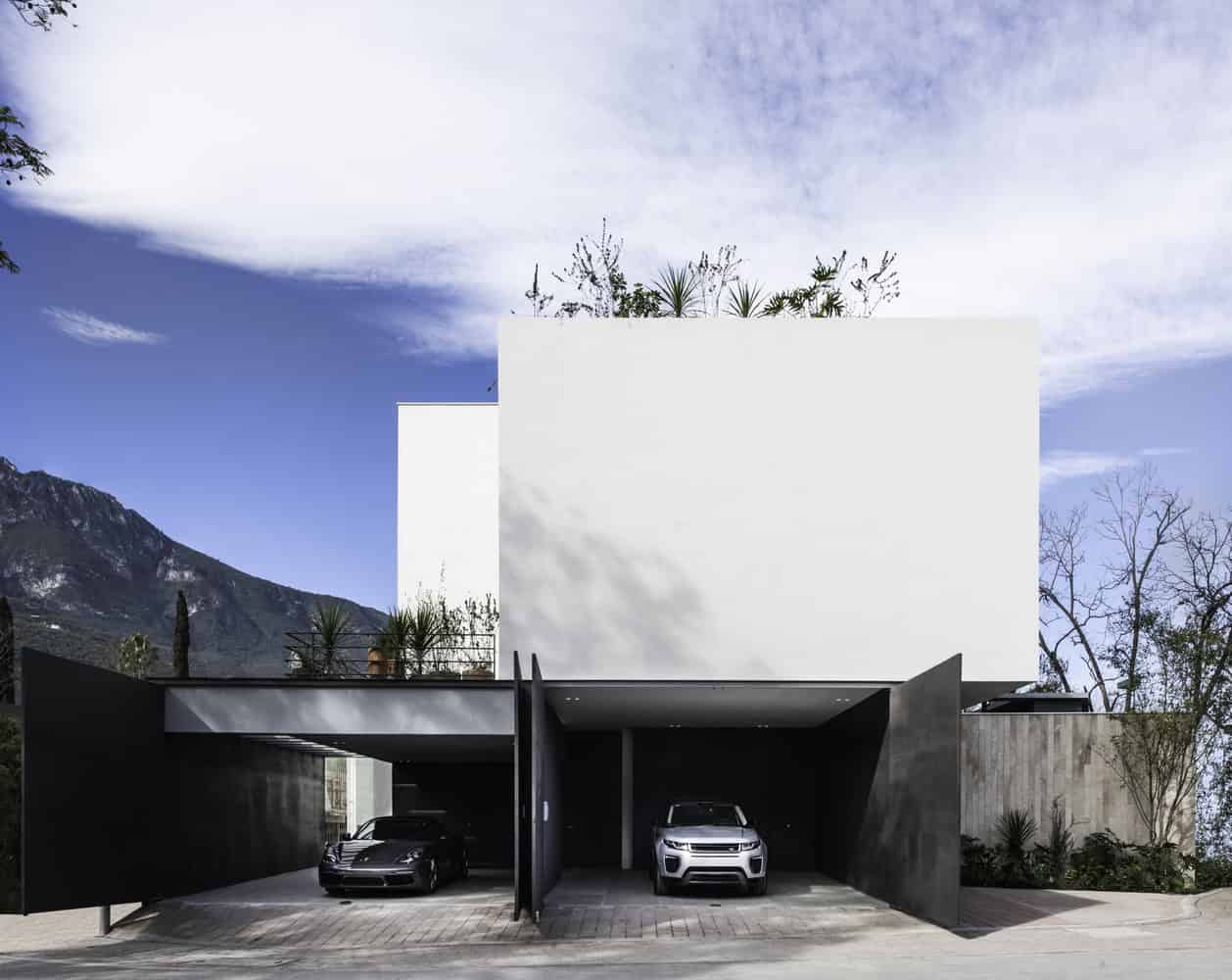 Modern minimalist house with sleek black garage doors, clean white exterior, and contemporary architectural design set against a mountainous backdrop.