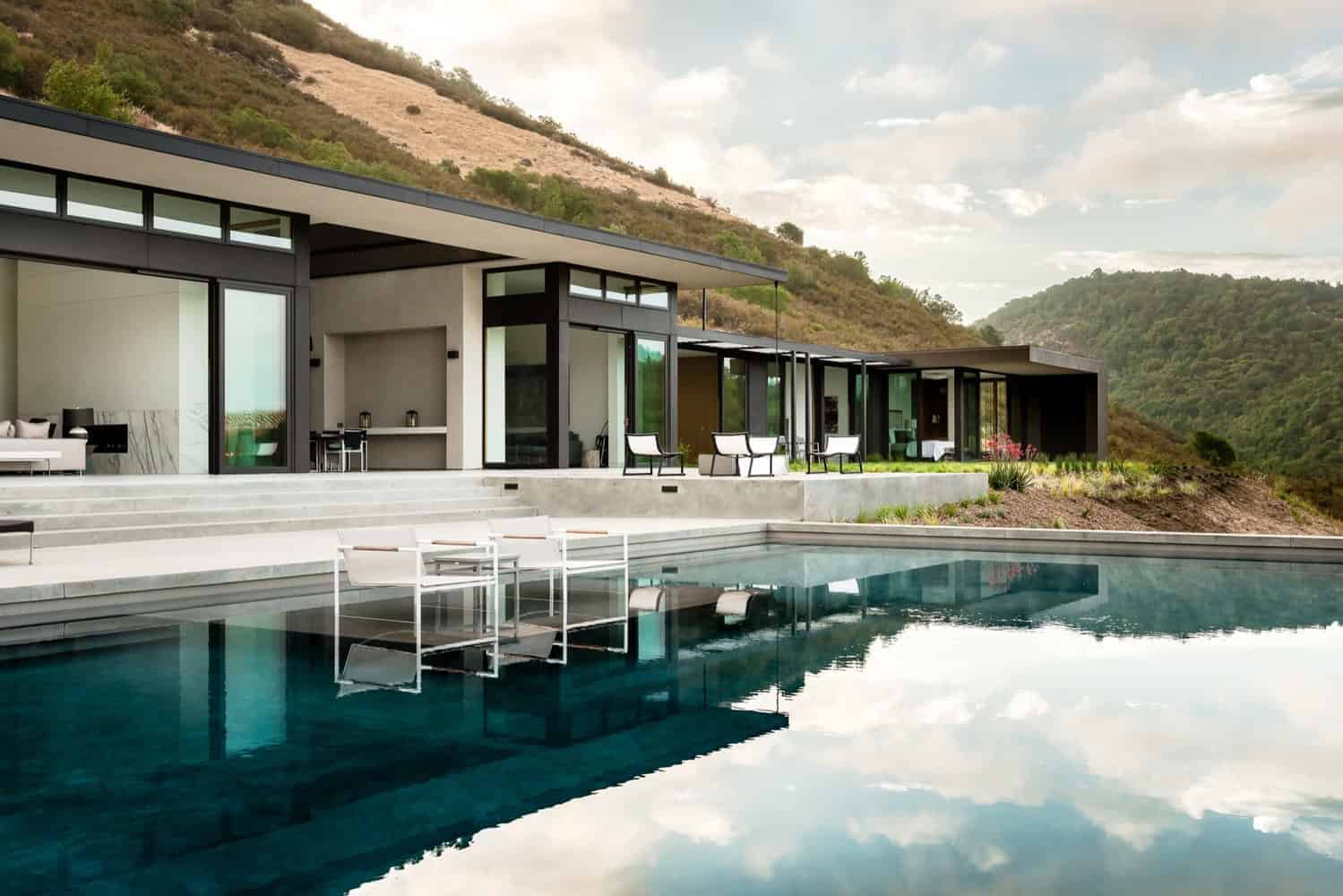 Modern luxury house with sleek design and large glass windows, featuring an outdoor pool, situated on a hillside with scenic mountain views. Perfect for contemporary architecture and outdoor living design.