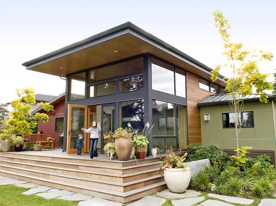 Contemporary modern house with large glass windows, wooden accents, and spacious outdoor steps, surrounded by lush greenery and potted plants, showcasing innovative architecture and stylish design.